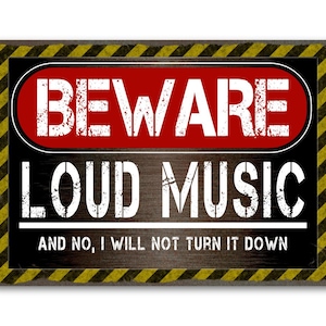 Könnte beinhalten: Rechteckiges Schild mit schwarzem Hintergrund und gelb-schwarzen Diagonalstreifen um den Rand. Das Schild lautet "BEWARE LOUD MUSIC" in weißer, verwitterter Schrift, mit dem Text "AND NO, I WILL NOT TURN IT DOWN" darunter.