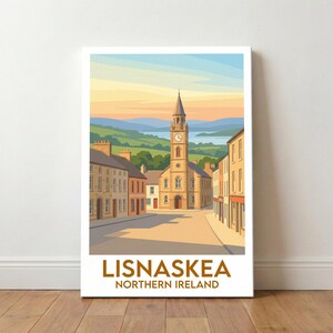 Puede incluir: Una impresión en lienzo que presenta una ilustración estilizada de Lisnaskea, Irlanda del Norte. La obra de arte representa una escena callejera con edificios, una torre del reloj y un paisaje escénico de colinas y un lago. La impresión tiene un borde blanco y el texto "LISNASKEA NORTHERN IRELAND".
