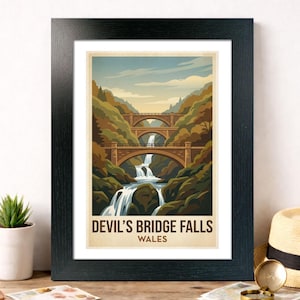 May include: Framed art print with a vintage illustration of Devil's Bridge Falls, Wales. The image shows a waterfall flowing under three stone bridges, set amidst green and brown trees. The text "DEVIL'S BRIDGE FALLS WALES" is at the bottom of the print.