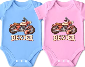Könnte beinhalten: Zwei kurzärmelige Babybodys, einer in Hellblau und einer in Hellrosa, jeweils mit einer grafischen Abbildung eines roten Motorrads mit braunem Sitz und passendem Helm, wobei der Name DEXTER in großen, cremefarbenen Buchstaben gedruckt ist.