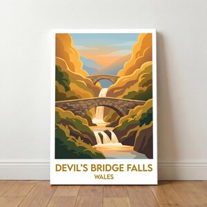 May include: A framed print depicting Devil's Bridge Falls in Wales. The image shows two stone bridges spanning a waterfall, surrounded by autumnal foliage and a sunset sky. The text at the bottom reads "Devil's Bridge Falls Wales."