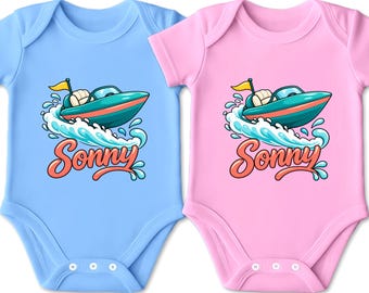 Könnte beinhalten: Zwei kurzärmelige Babybodys, einer in Hellblau und einer in Hellrosa, jeweils mit einer Grafik eines türkisfarbenen Schnellboots auf einer Welle, einer gelben Flagge und dem Namen Sonny in orangefarbener Schreibschrift unter dem Boot.