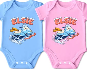 Könnte beinhalten: Zwei kurzärmelige Babybodys, einer in Hellblau und einer in Hellrosa, jeweils mit einer Grafik eines Cartoon-Schneemobils mit gelbem Schal und dem Namen ELSIE in orangefarbenen Buchstaben darüber, mit Schneegestöber am unteren Rand.