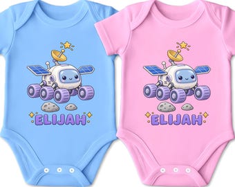 Könnte beinhalten: Zwei kurzärmelige Babybodys, einer in Hellblau und einer in Hellrosa, jeweils mit einer Grafik eines lächelnden Cartoon-Weltraumrovers mit Solarzellen, einer Satellitenschüssel und zwei kleinen Steinen. Der Name ELIJAH ist lila aufgedruckt.