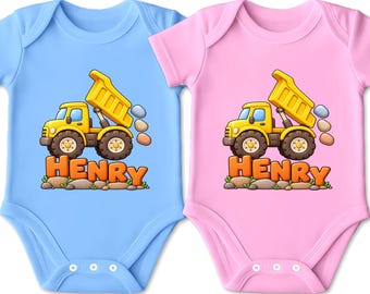 Könnte beinhalten: Zwei kurzärmelige Babybodys, einer in Hellblau und einer in Hellrosa, jeweils mit einer Grafik eines gelben Muldenkippers, der Steine über dem orangefarbenen Schriftzug HENRY ablädt, der auf kleinen grauen und braunen Steinen ruht.