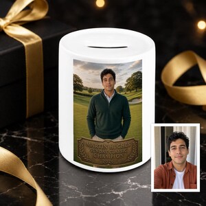 May include: A white ceramic money box featuring a printed photograph of a person wearing a dark green quarter-zip sweater on a golf course. Below the image is a bronze-colored plaque graphic with the text MARTIN HUGHES SUNDAY CLASSIC CHAMPION 2026.
