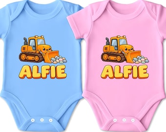 Könnte beinhalten: Zwei kurzärmelige Babybodys, einer in Hellblau und einer in Hellrosa, jeweils mit einem orangefarbenen Cartoon-Bulldozer, der einen Haufen bunter Steine schiebt, und dem Namen ALFIE in großen gelben Buchstaben mit dunkler Umrandung.