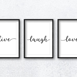 Könnte beinhalten: Drei schwarze gerahmte Drucke mit weißen Hintergründen und schwarzer Kalligraphie. Die Drucke lauten "live", "laugh" und "love".