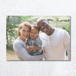 Pu&ograve; includere: Un ritratto di famiglia di una coppia di razze miste e il loro giovane figlio. I genitori sorridono e guardano la fotocamera. Il figlio &egrave; tenuto dalla madre e guarda la fotocamera. La famiglia &egrave; in piedi in una zona boscosa.
