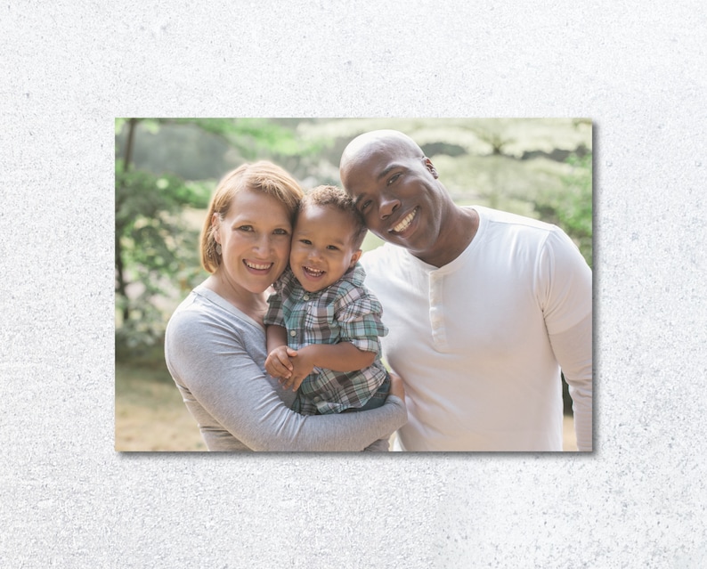 Pu&ograve; includere: Un ritratto di famiglia di una coppia di razze miste e il loro giovane figlio. I genitori sorridono e guardano la fotocamera. Il figlio &egrave; tenuto dalla madre e guarda la fotocamera. La famiglia &egrave; in piedi in una zona boscosa.