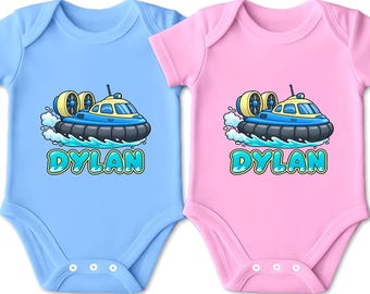 Könnte beinhalten: Zwei kurzärmelige Babybodys, einer in Hellblau und einer in Hellrosa, jeweils mit einer Cartoon-Illustration eines blau-gelben Luftkissenfahrzeugs auf Wasserwellen und dem Namen DYLAN in großen, blubbernden, hellblauen Buchstaben darunter.