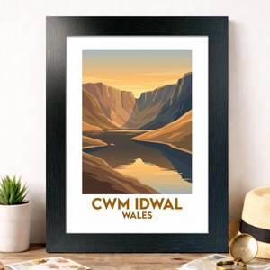 May include: A framed print depicting Cwm Idwal in Wales. The artwork shows a lake nestled between mountains, with a sunset sky. The print is in a black frame and has the text "CWM IDWAL WALES" at the bottom.