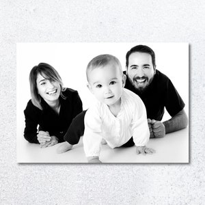 Pu&ograve; includere: Una fotografia in bianco e nero di una famiglia con una madre, un padre e un bambino. La madre sorride e guarda la fotocamera. Il padre sorride e guarda la fotocamera. Il bambino sta gattonando verso la fotocamera.