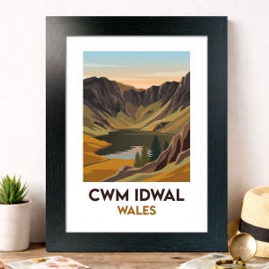 May include: Framed print depicting Cwm Idwal, Wales. The landscape art shows a lake nestled between mountains in brown, green, and orange hues. The sky gradients from blue to orange. The text "CWM IDWAL WALES" is at the bottom.
