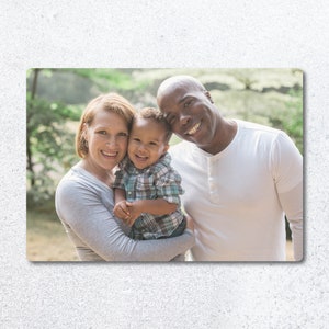 Pu&ograve; includere: Un ritratto di famiglia di una coppia e il loro giovane figlio. I genitori sorridono e guardano la fotocamera. Il figlio &egrave; tenuto dalla madre e guarda la fotocamera. La famiglia &egrave; in piedi davanti a uno sfondo verde.