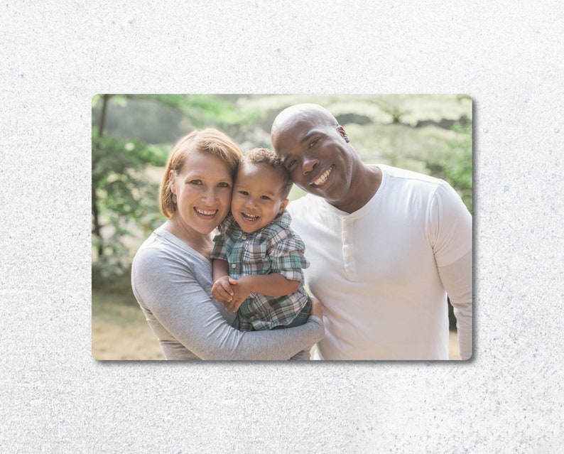 Pu&ograve; includere: Un ritratto di famiglia di una coppia e il loro giovane figlio. I genitori sorridono e guardano la fotocamera. Il figlio &egrave; tenuto dalla madre e guarda la fotocamera. La famiglia &egrave; in piedi davanti a uno sfondo verde.