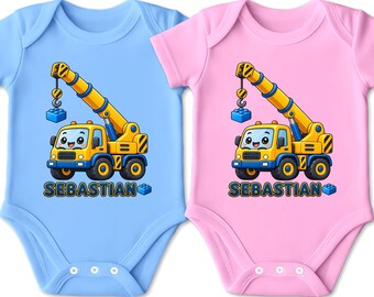 Könnte beinhalten: Zwei kurzärmelige Babybodys, einer in Hellblau und einer in Hellrosa, jeweils mit einer Grafik eines gelben Kranwagens mit lächelndem Gesicht und dem Namen SEBASTIAN in dunkelblauen Buchstaben neben einem kleinen blauen Baustein.