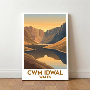 May include: A framed art print depicting a tranquil lake scene nestled between high mountains, set against a warm sunset. The print displays the text "CWM IDWAL WALES" in a brown font at the bottom.