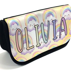 Könnte beinhalten: Schwarzes Federmäppchen mit einem bunten Regenbogen- und Wolkenmuster. Der Name "OLIVIA" ist in großen Pastellbuchstaben aufgedruckt. Geeignet für Stifte, Bleistifte und andere Schreibwaren.