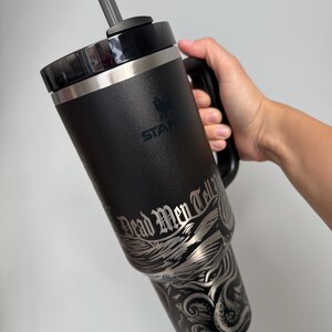K&ouml;nnte beinhalten: Schwarze Reise-Thermoskanne aus Edelstahl mit schwarzem Griff und klarem Strohhalm. Die Kanne hat ein silbernes Design mit einem Kraken und Wellen mit dem Text "Dead Men Tell No Tales".