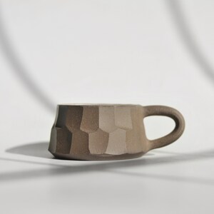 May include: A brown ceramic mug with a textured, geometric design. The mug has a rounded handle.