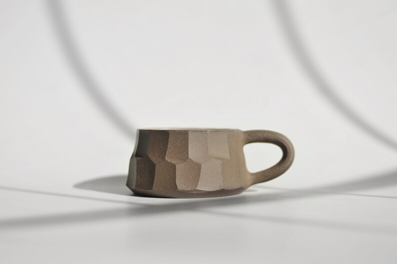 May include: A brown ceramic mug with a textured, geometric design. The mug has a rounded handle.