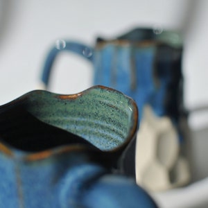 Puede incluir: Dos tazas de cer&aacute;mica azul con un esmalte moteado. Las tazas tienen un dise&ntilde;o ondulado &uacute;nico y est&aacute;n parcialmente enfocadas.