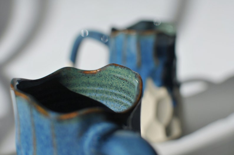 Puede incluir: Dos tazas de cer&aacute;mica azul con un esmalte moteado. Las tazas tienen un dise&ntilde;o ondulado &uacute;nico y est&aacute;n parcialmente enfocadas.
