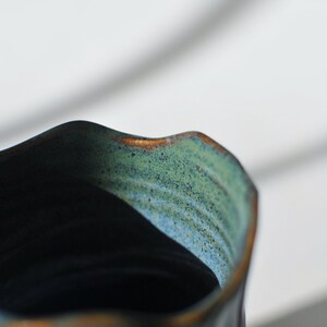 Puede incluir: Primer plano del interior de una taza de cer&aacute;mica azul oscuro con un esmalte verde y marr&oacute;n. La taza tiene un borde ondulado.