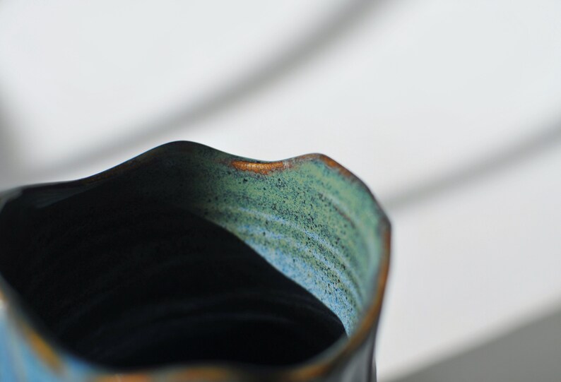 Puede incluir: Primer plano del interior de una taza de cer&aacute;mica azul oscuro con un esmalte verde y marr&oacute;n. La taza tiene un borde ondulado.