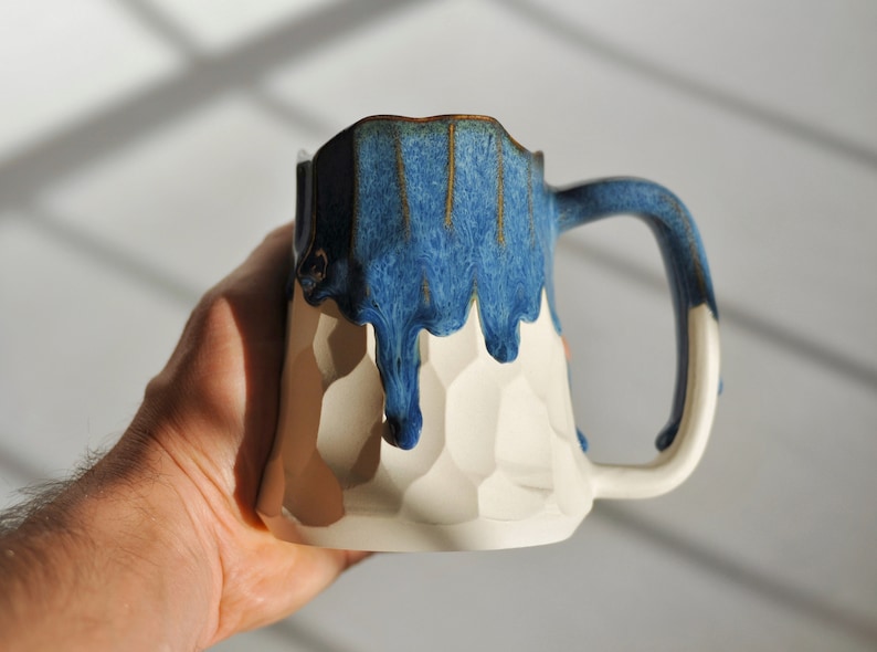 Puede incluir: Una taza de cer&aacute;mica blanca con un esmalte azul que gotea por los lados. La taza tiene un dise&ntilde;o texturizado, similar a un panal de abejas.