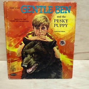 May include: A vintage book cover for "Gentle Ben and the Pesky Puppy." The cover features a boy with blond hair, resting his chin on a black bear. The title is in large blue letters, with the author's name and the book's title visible.