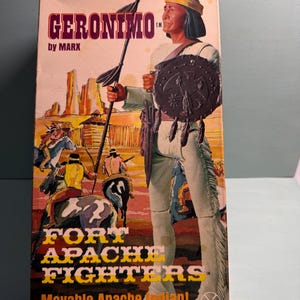 Op de afbeelding: Vintage "Geronimo" speelgoeddoos van Marx. De doos toont een afbeelding van Geronimo met een speer en schild, met de woorden "Fort Apache Fighters" en "Movable Apache Indian!" erop gedrukt.