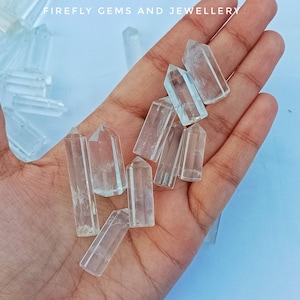 May include: A collection of clear quartz crystal points, also known as rock crystals, in various sizes. The crystals are pointed at one end and have a smooth, polished surface. The crystals are arranged in a hand, with the points facing upwards.