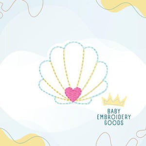 Op de afbeelding: Geborduurd zeeschelpontwerp met een roze hart in het midden. De schelp is omlijnd in lichtblauw met gele stiksels. De tekst "BABY EMBROIDERY GOODS" staat onder een gele kroon.