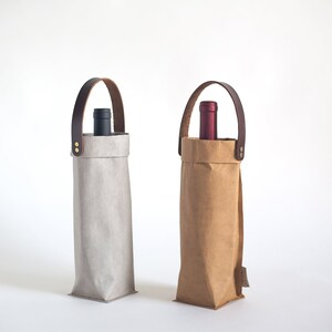 May include: Two wine bottle carriers made of brown paper and gray fabric with leather handles. The carriers have a bottle of wine inside.