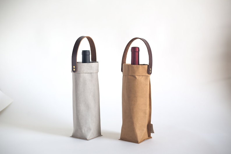 May include: Two wine bottle carriers made of brown paper and gray fabric with leather handles. The carriers have a bottle of wine inside.