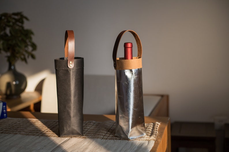 May include: Two wine bottle carriers with leather handles. One is black and the other is silver.