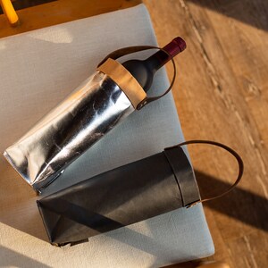May include: Two wine bottle carriers, one silver and one black, with leather handles.