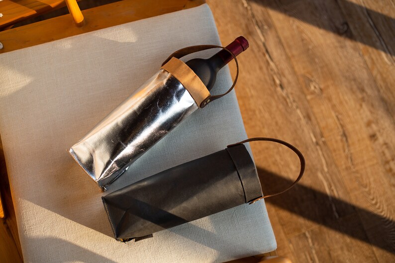 May include: Two wine bottle carriers, one silver and one black, with leather handles.