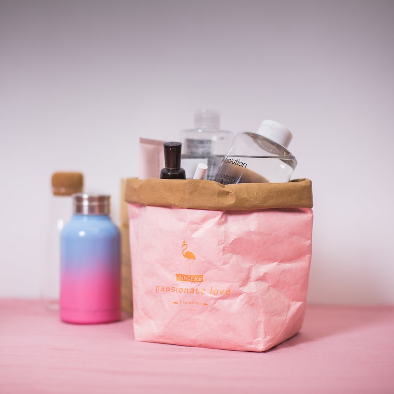 May include: A pink paper bag with a brown top, filled with various bottles and tubes of toiletries. The bag has a flamingo logo and the text "SINCERE passionate love Flamingo".