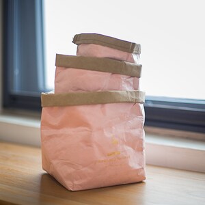 May include: Three pink paper bags with brown paper handles stacked on top of each other. The bottom bag has the text "passionate love" printed on it.