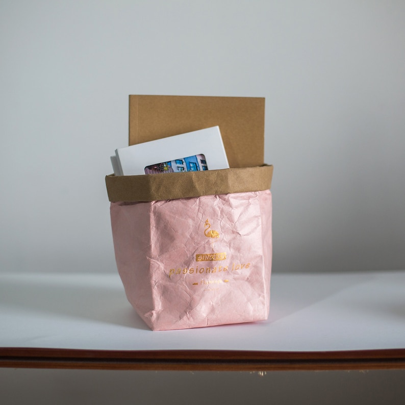 May include: A pink paper bag with a gold flamingo logo and the text "Ginger Passion Made Love" in gold. The bag is filled with white envelopes and a brown envelope.