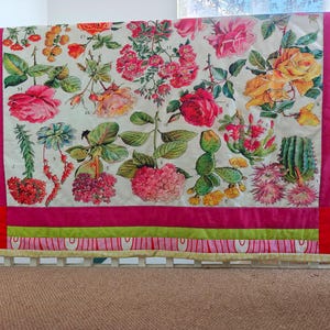 May include: A floral quilt with a botanical print of various flowers and plants in shades of pink, red, yellow, and green. The quilt has a white background with a pink, green, and red border. The quilt is displayed on a white cot.