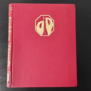 May include: A red hardback book with the title "Golden Hands" in gold lettering on the spine. The front cover features a gold illustration of two hands sewing.