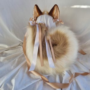 May include: A fox cosplay kit with brown and tan faux fur ears, a fluffy tail, and a white head covering. The ears have darker brown tips and small bows. The tail is a mix of white and tan fur, with ribbons.