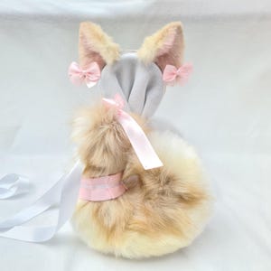 Könnte beinhalten: Ein Plüschfuchs-Schwanz mit einem weißen Band und einer rosa Schleife. Der Schwanz besteht aus weichem, flauschigem Fell und ist perfekt, um jedem Outfit einen Hauch von Verspieltheit zu verleihen.