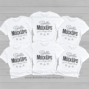 May include: Six white t-shirts with the text "Bella Mockups" and "your design here" printed on them. The shirts are arranged in a stack on a gray wooden surface.