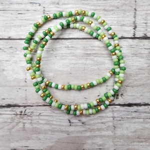 May include: A green, white, and gold beaded necklace. The necklace is made of small, round beads and is layered in a triple strand.