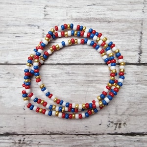 May include: A beaded waist chain featuring red, white, blue, and gold beads. The beads are strung together to form a long, flexible strand. The waist chain is designed to be worn around the waist as a decorative accessory.